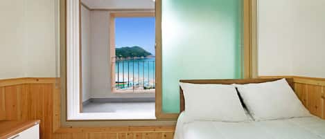 A bedroom with a bed, a wooden dresser, and a view of a beach through an open door.