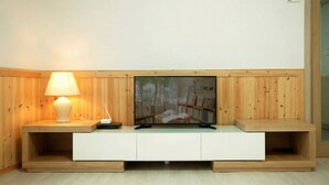 A modern living room with a wooden panel wall, a white entertainment unit, a lamp, and a flat-screen TV. - Samcheok Haega Pension (Samcheok)