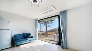 A modern room with a sofa, a ceiling fan, and a view of a deck with outdoor furniture. - Gyeongju Hyu Plus Pension (Gyeongju)