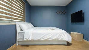 Un dormitorio con cama, mesita de noche, televisor de pared y ventana con persianas.