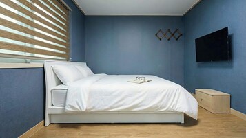 A bedroom with a bed, a bedside table, a wall-mounted TV, and a window with blinds.