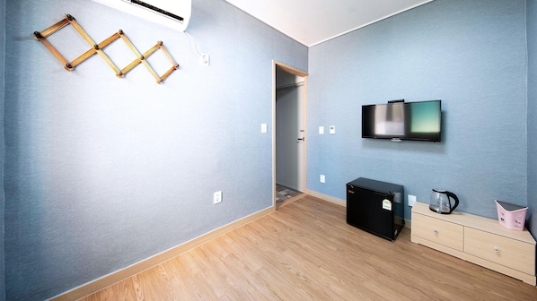 Quarto moderno com televisão de tela plana, um pequeno frigorífico e um armário de madeira.