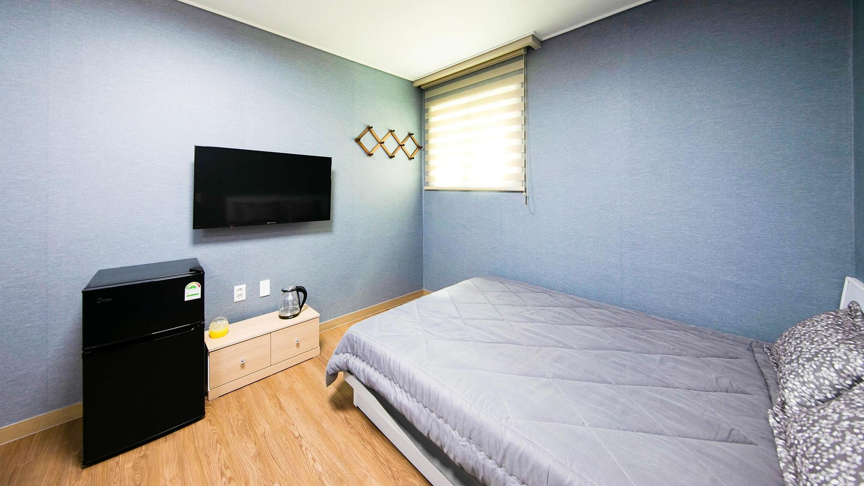 Un dormitorio con cama, televisor, refrigerador pequeño y cómoda de madera.