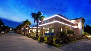 A modern hotel with a brick facade, large windows, and a covered outdoor area with palm trees. - Seogwipo Sungsan Golden Village Pension (Seogwipo)