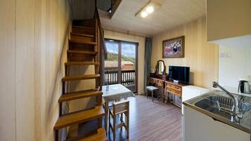 A cozy kitchen with wooden floors, a dining table, a TV, and a sink.