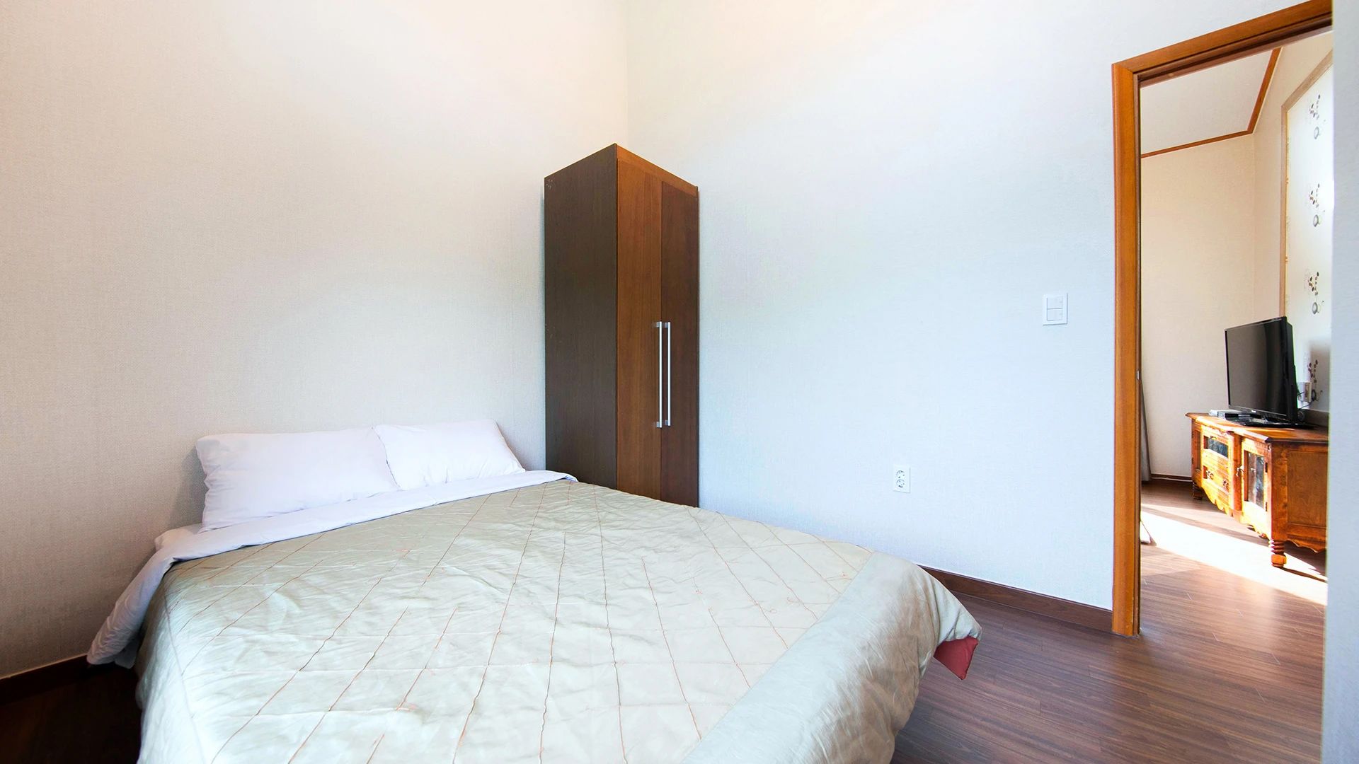 A bedroom with a bed, a wardrobe, and a television in the corner.