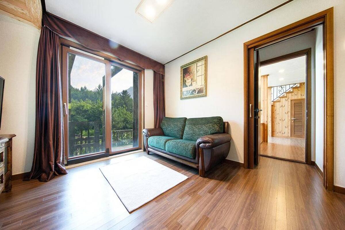 Une pièce spacieuse dotée d’une porte-fenêtre coulissante donnant sur un balcon, d’un canapé vert et d’un plancher en bois.
