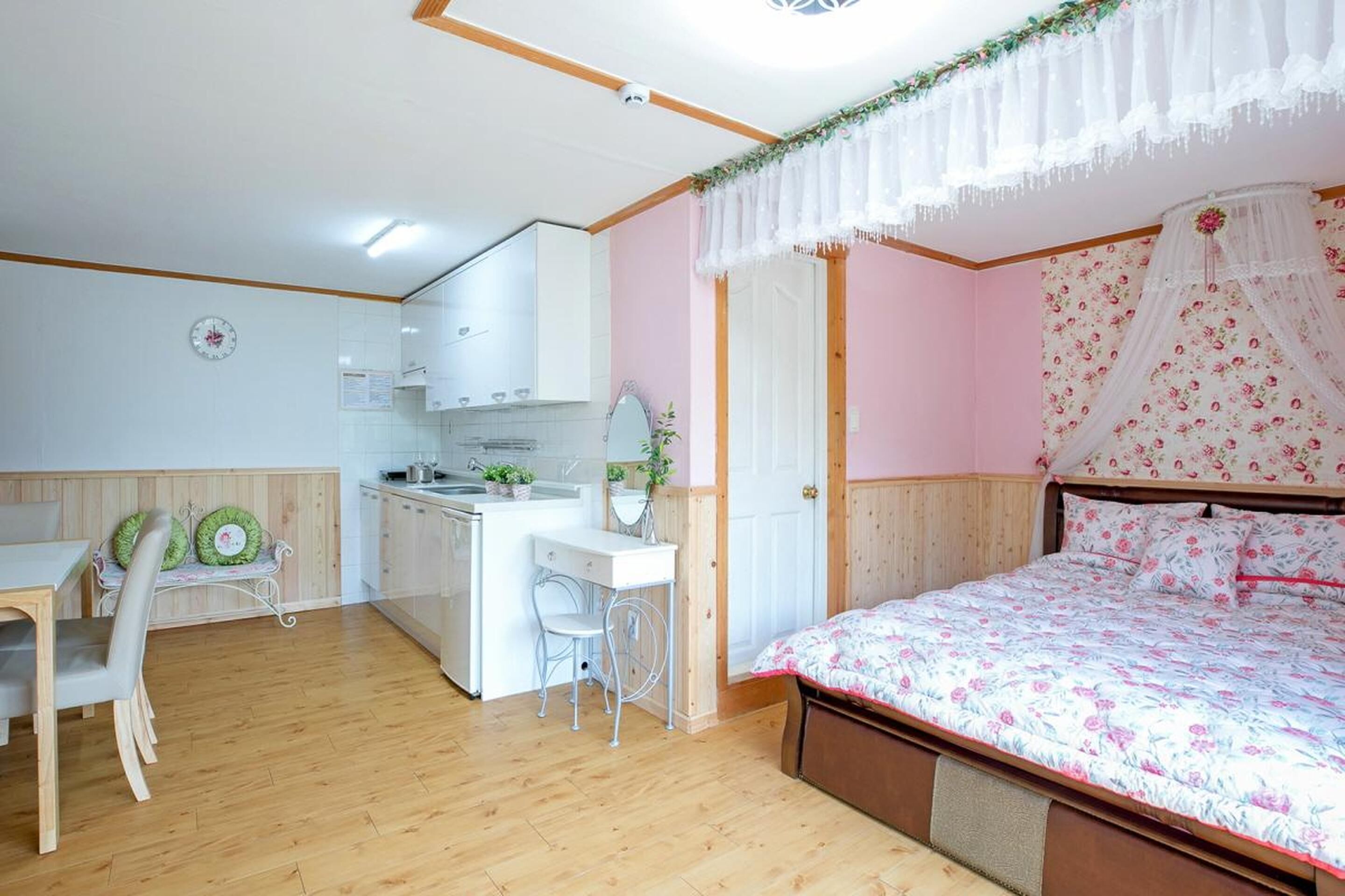 A bedroom with a canopy bed, a small kitchenette, a dining table, and a chair.