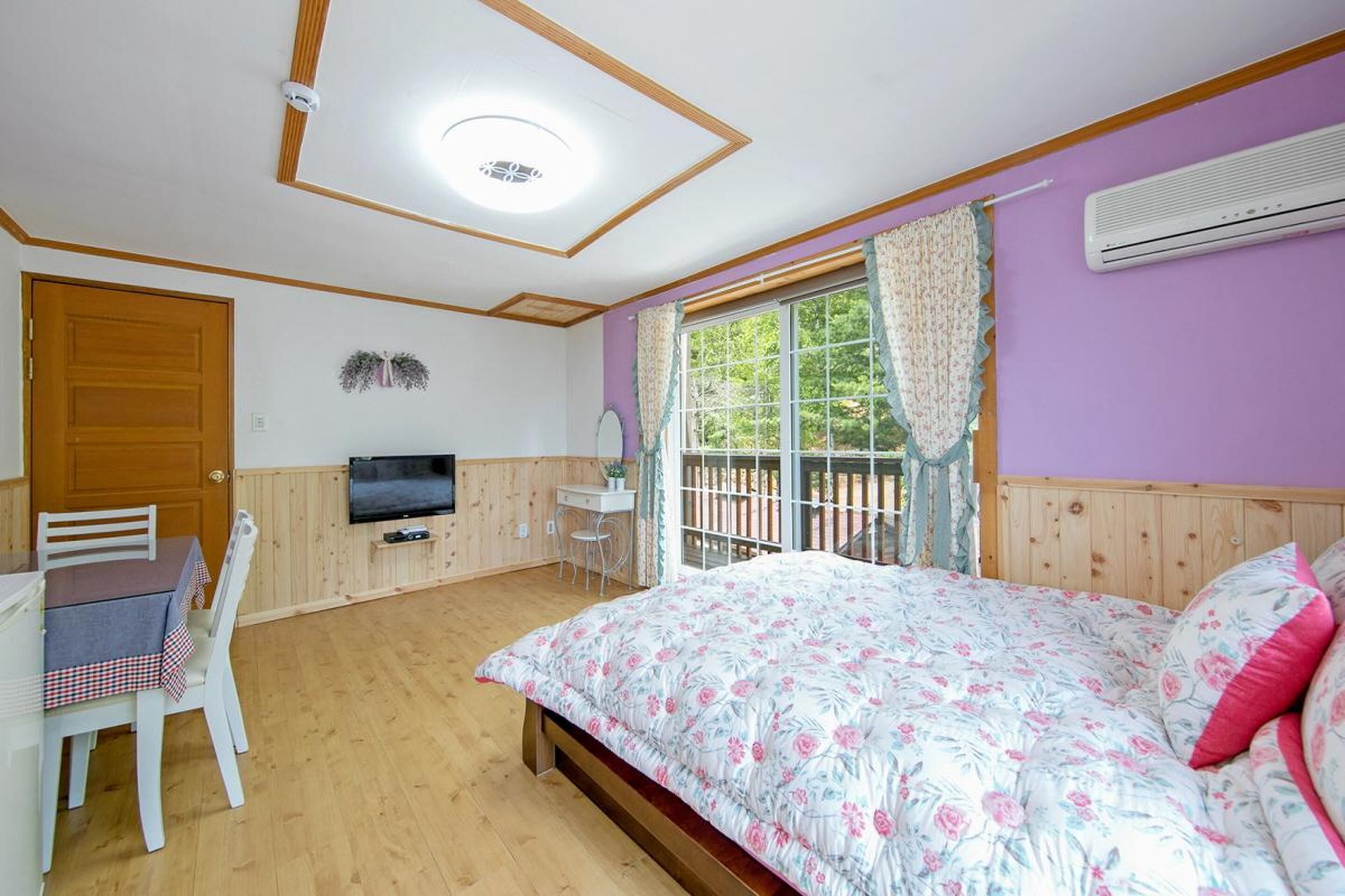A room with a bed, a TV, a desk, and a window with curtains.