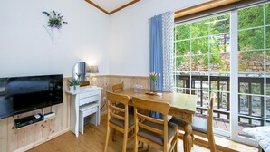 Ein gemütliches Zimmer mit Holztisch, Stühlen, einem Fernseher und einem Fenster mit Blick auf Grünflächen.