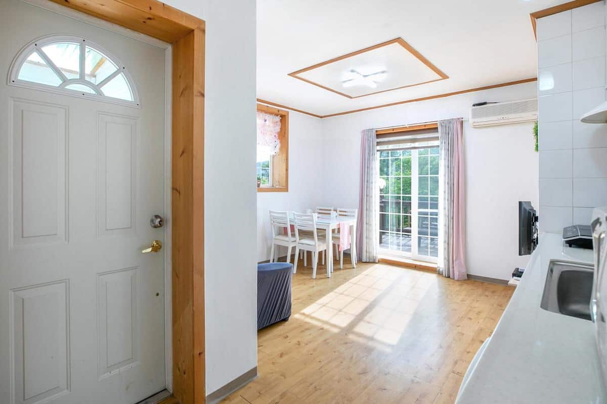 Une cuisine avec un plancher en bois, une porte blanche et un coin repas comprenant une table et des chaises.