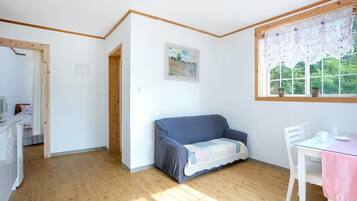 A room with a wooden floor, a blue sofa, a white table with a pink tablecloth, and a window with a floral curtain.