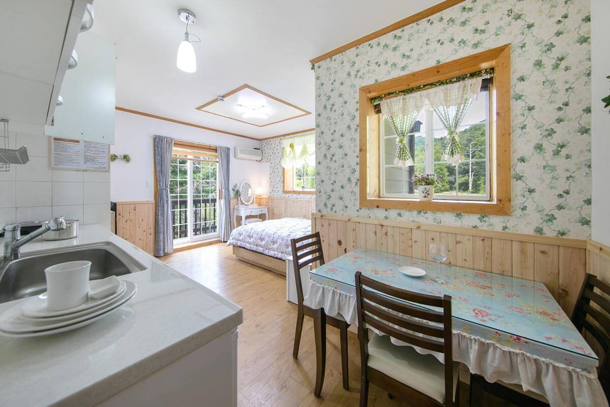 Une cuisine équipée d’un évier, un coin repas avec une table et des chaises, et une fenêtre donnant sur un paysage verdoyant.