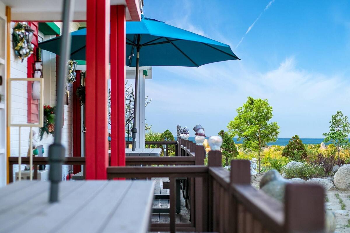 En träveranda med ett blått parasoll, utsikt över havet och en byggnad med färgglada väggar.