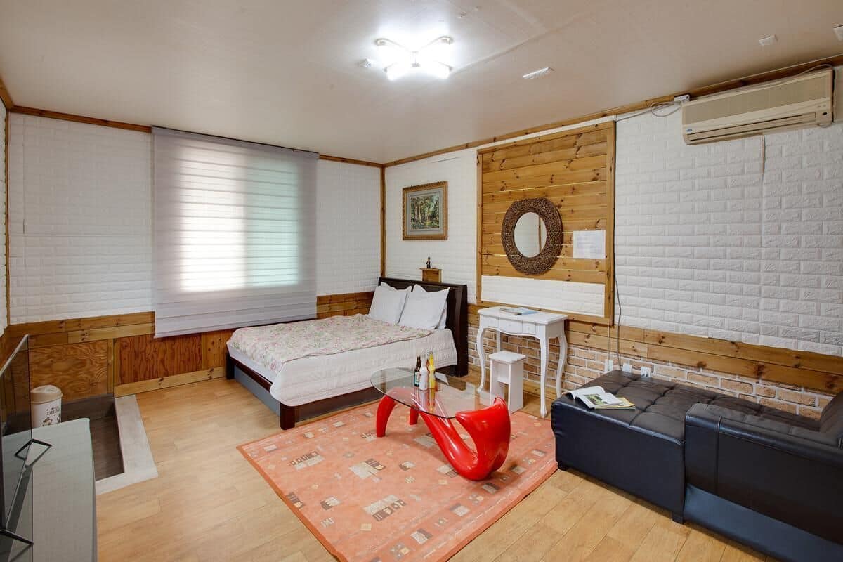 A bedroom with a bed, a desk, a chair, a sofa, and a wall-mounted air conditioner.