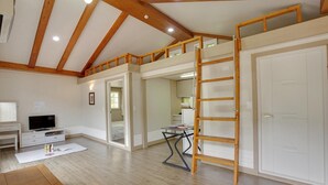 A spacious room with a loft area, wooden beams, a TV, and a desk.