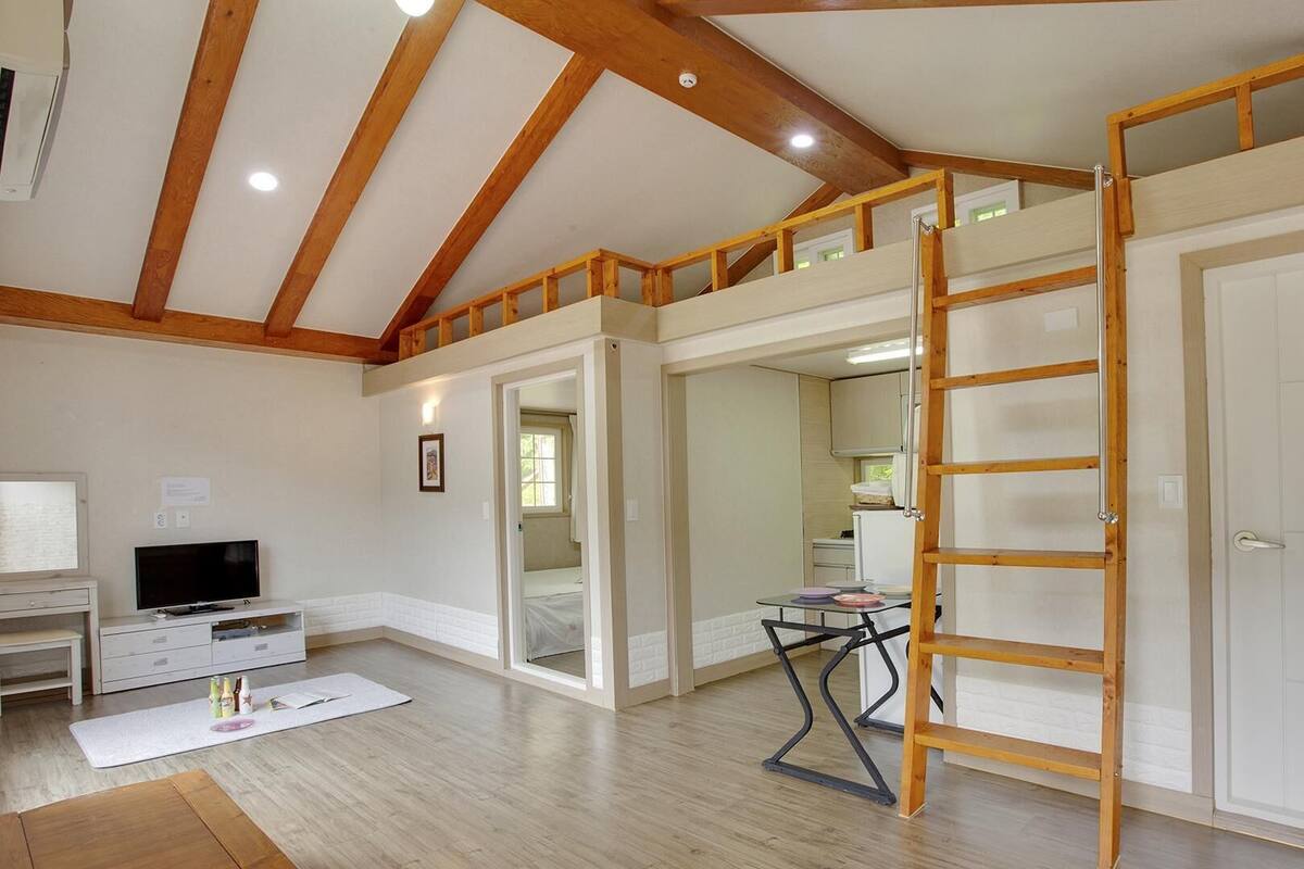 A spacious room with a loft area, wooden beams, a TV, and a desk.