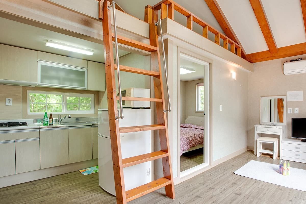 A compact, modern apartment with a kitchenette, a bedroom with a bed and a window, a bathroom with a mirror and a toilet, and a TV in the living area.