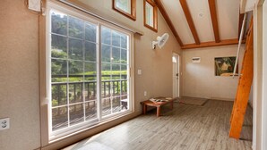 A room with large windows, wooden beams, a fan, and a table with magazines.