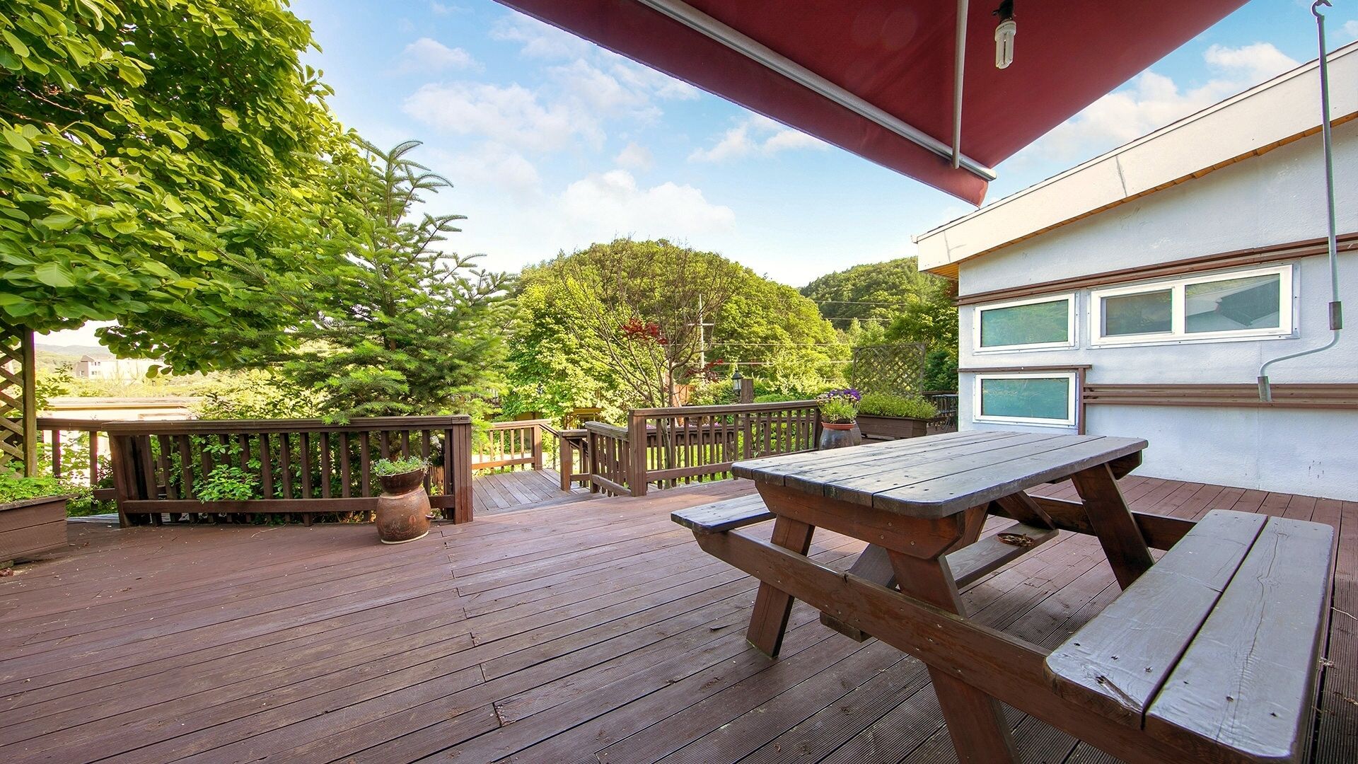 Una terraza de madera con una mesa de picnic y un toldo rojo.