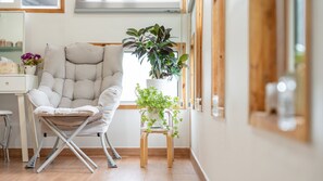 A modern room with a cushioned chair, a small wooden stool with a plant, and a window with blinds. - Hongcheon Lime Orange Pension (Hongcheon)