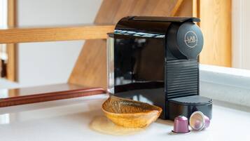 Eine Kaffeemaschine mit Glasbehälter, eine Holzschale und zwei Metalltassen auf einer Küchenarbeitsplatte.