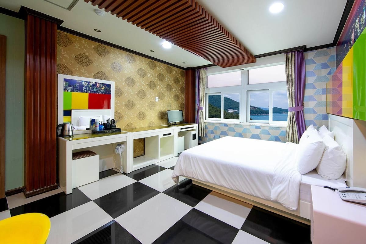 A hotel room with a bed, a desk, a chair, a phone, and a window with a view.