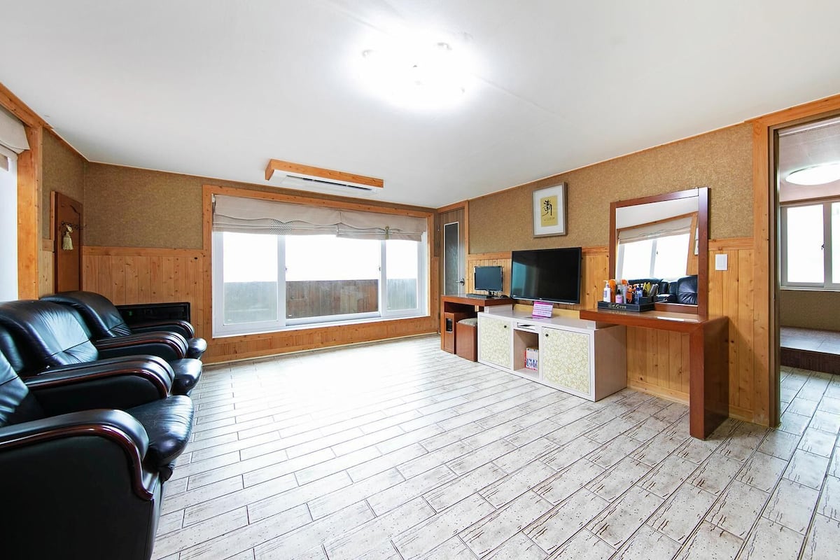 A room with a wooden floor, a TV, a desk with a computer, and a seating area with leather chairs.