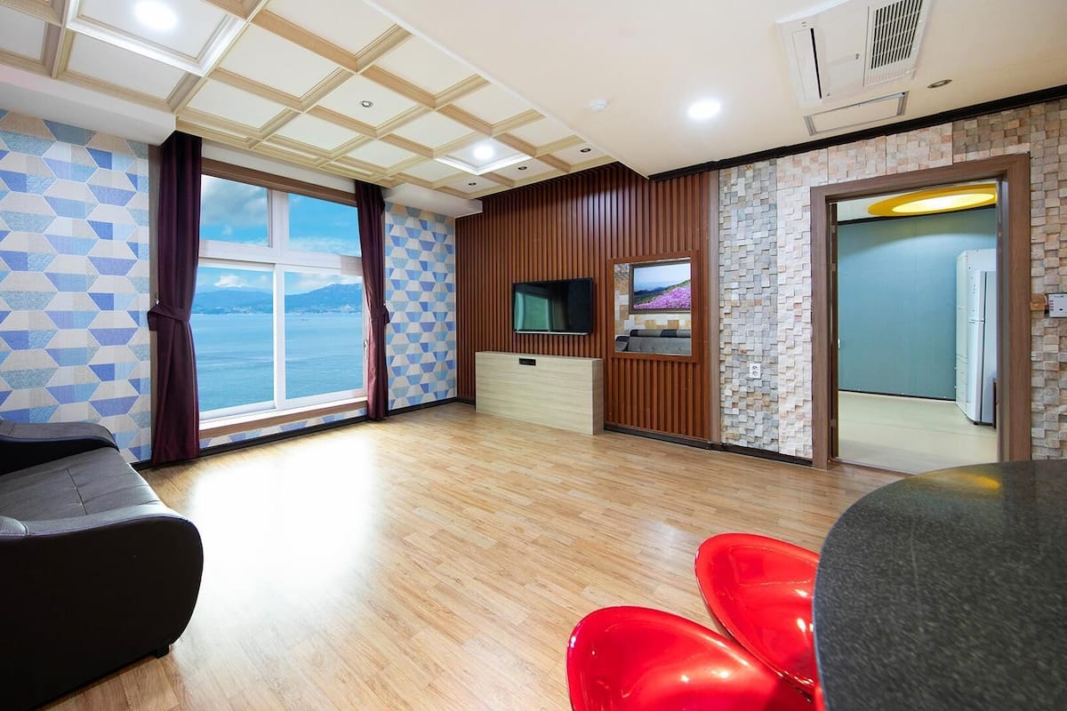 A modern living room with a sofa, a TV, and a view of the sea.