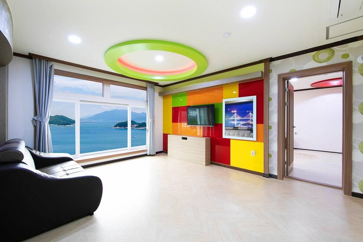 A modern hotel room with a large window offering a scenic view of the sea and mountains.