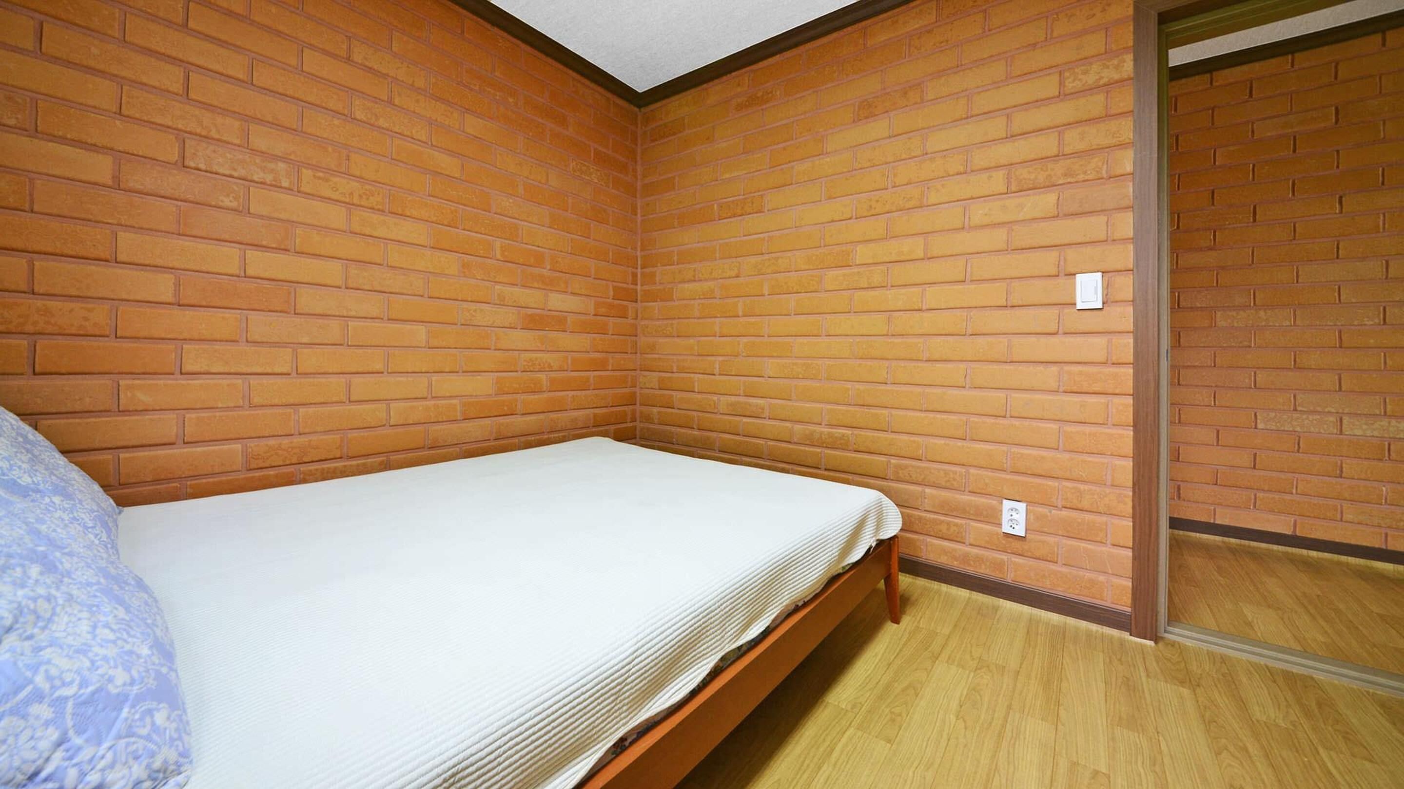 Pequeña habitación individual con paredes de ladrillo y suelo de madera.