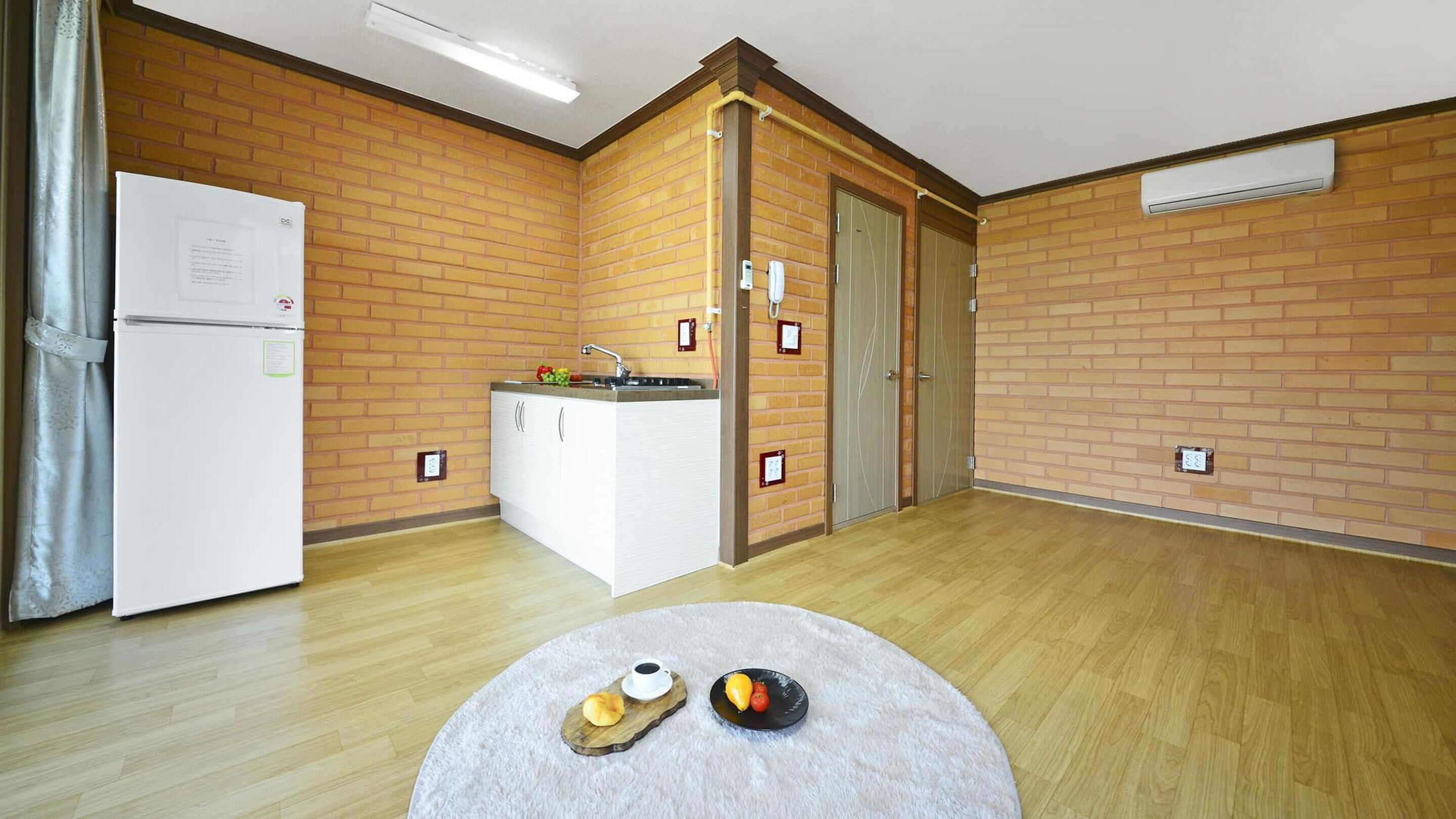 Een compacte keuken met een koelkast, een spoelbak en een klein eiland. Er staat een ronde tafel met een bord eten en een beker.