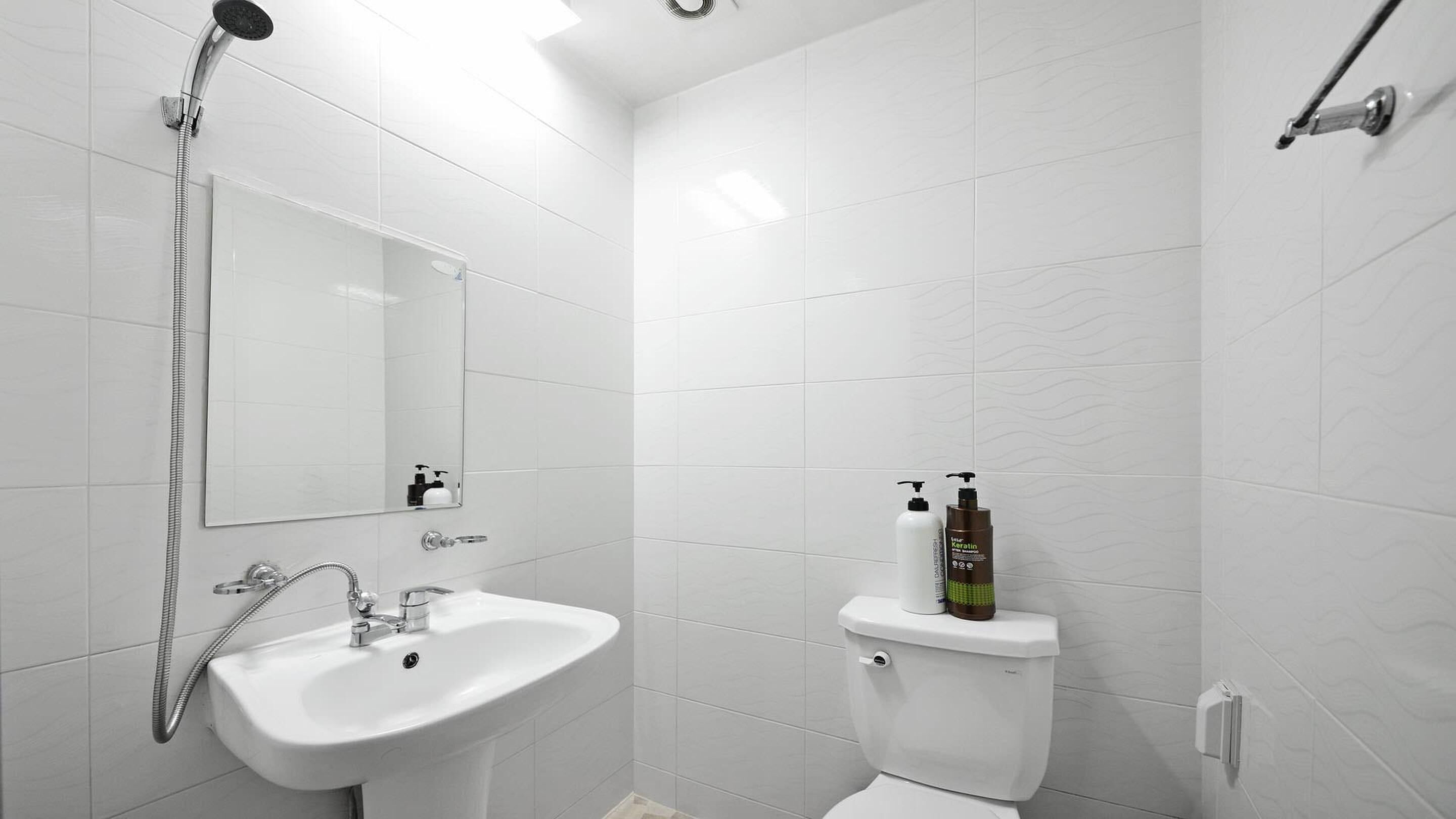 A modern bathroom with a white sink, a mirror, a shower, and a toilet.