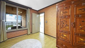 Una habitación con un gran ventanal corredero que da a un balcón, un armario de madera con tiradores decorativos y una alfombra blanca en el suelo.