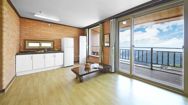 Una cocina con piso de madera, gabinetes blancos, un refrigerador y una ventana con vista a un balcón y al cielo y árboles.