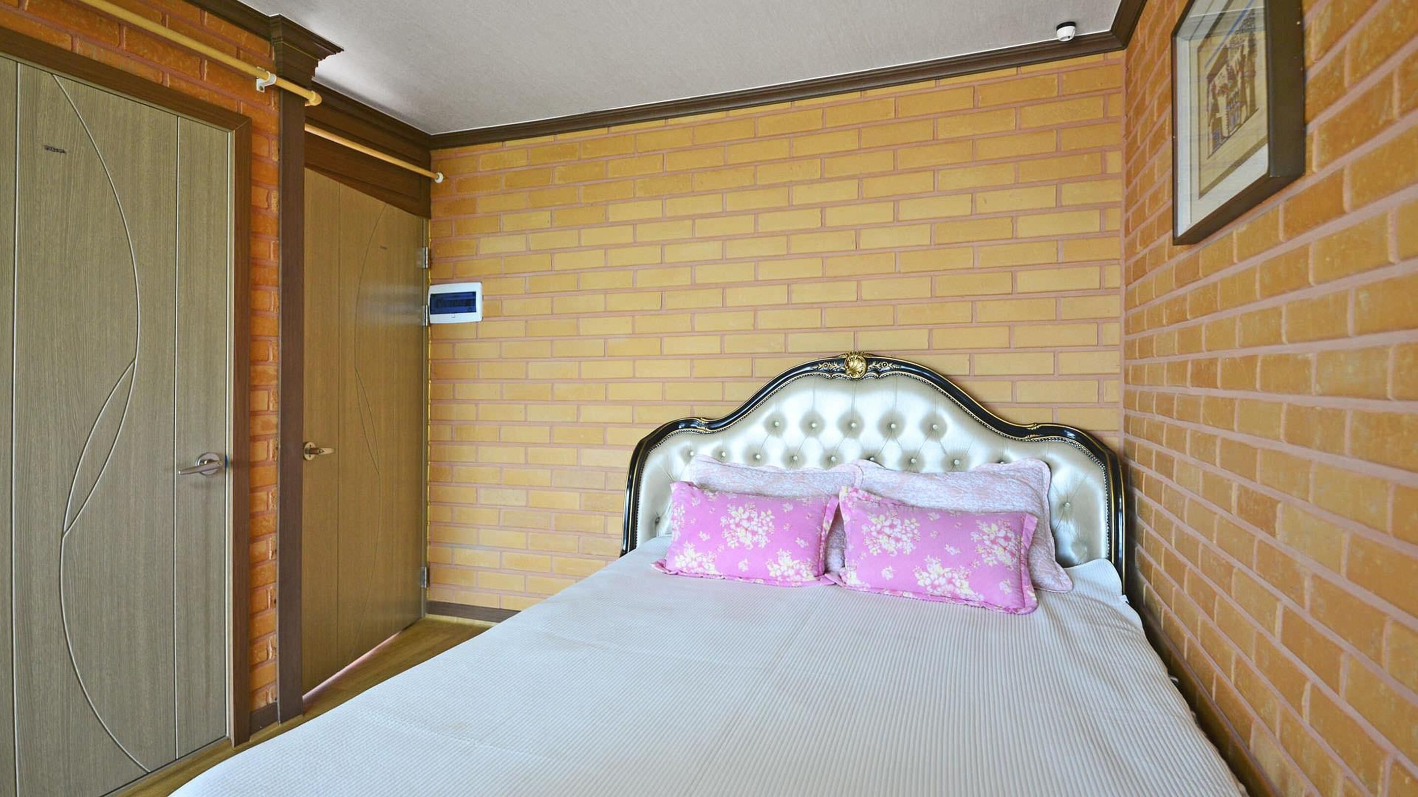 A bedroom with a bed, a wooden wardrobe, and a brick wall.