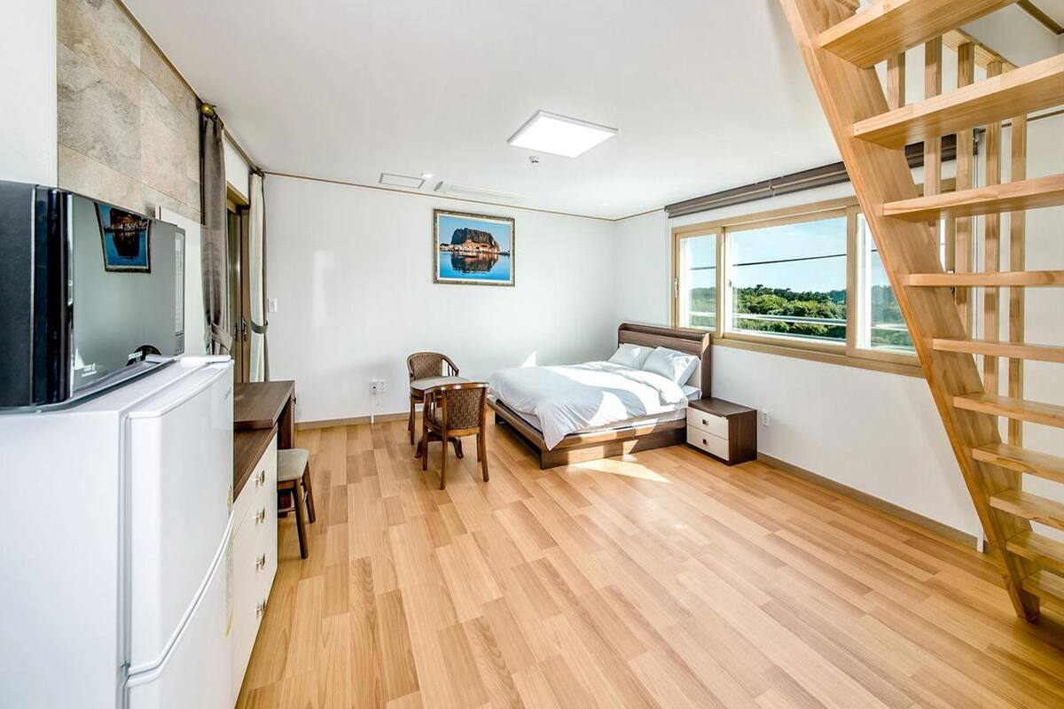 Ein Schlafzimmer mit Bett, Schreibtisch, Stuhl, Fernseher und einem Fenster mit Blick.