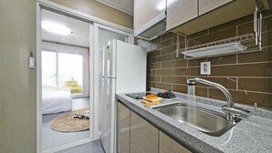 Een kleine keuken met een inbouwkoelkast, een spoelbak met een moderne kraan en een raam met uitzicht op een balkon.