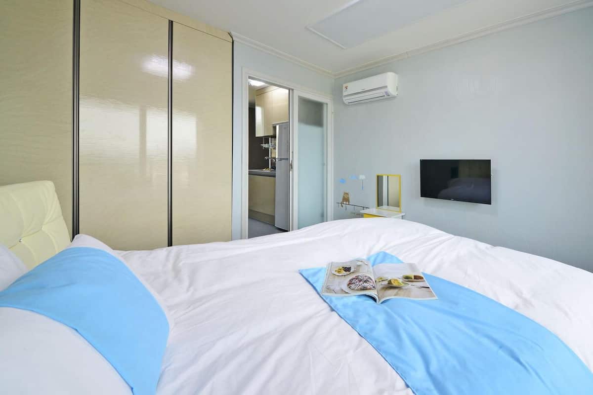 Une chambre d’hôtel équipée d’un lit, d’une télévision, d’un appareil de climatisation et d’une salle de bain visible à travers une porte ouverte.
