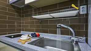 Una cocina con un lavamanos de acero inoxidable, una cafetera, un frutero y un tendedero sobre el lavamanos.