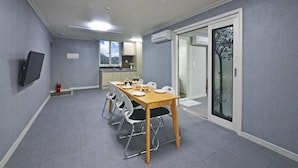 Een eetgedeelte met een lange tafel, stoelen en een televisie aan de muur.
