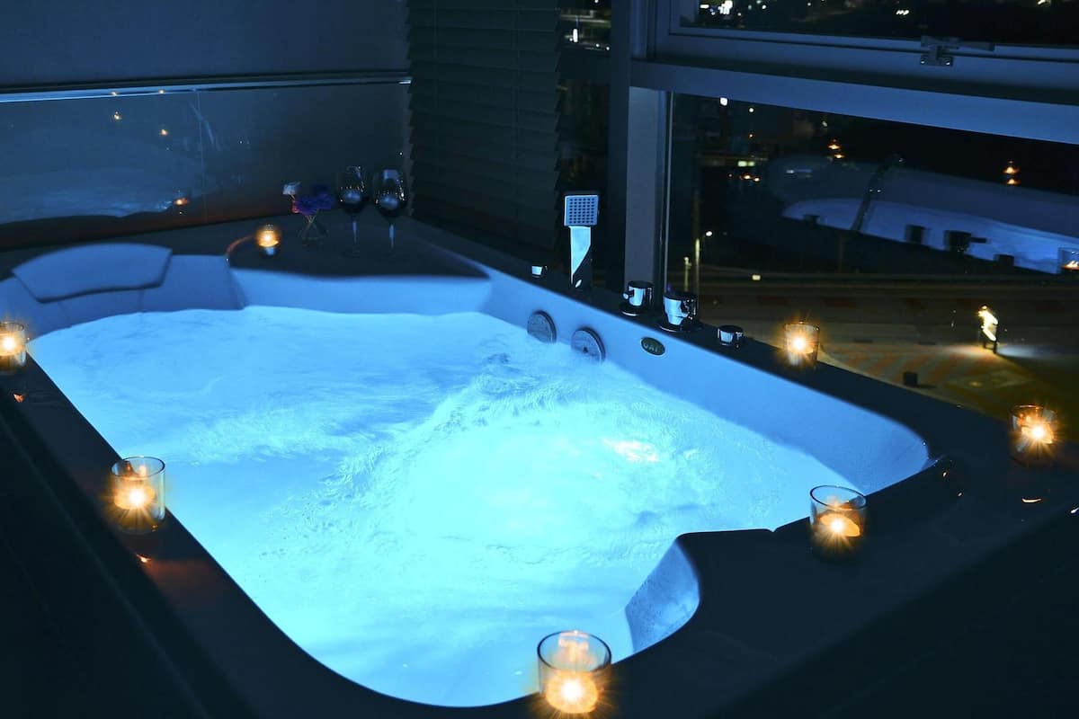 Un bain à remous entouré de bougies, une fenêtre et une vue sur la ville.