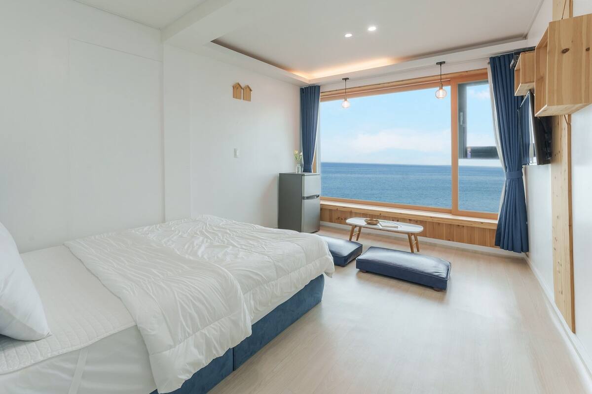Een slaapkamer met een bed, een klein tafeltje en uitzicht op zee.