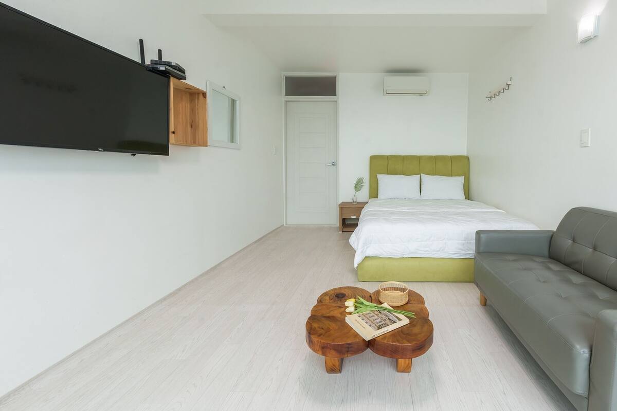 Een moderne, compacte kamer met een bed, een grijze bank en een houten salontafel.