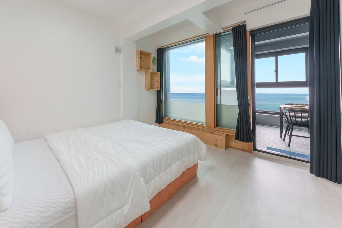 Hotelkamer met een bed, houten hoofdeinde, kleine televisie en balkon met tafel en stoelen.