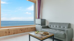 Quarto com vista para o mar, um sofá cinzento, uma pequena mesa com um livro e flores, e um armário branco.