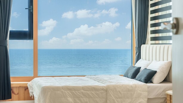Quarto com cama, vista para o mar e janela com cortinas.