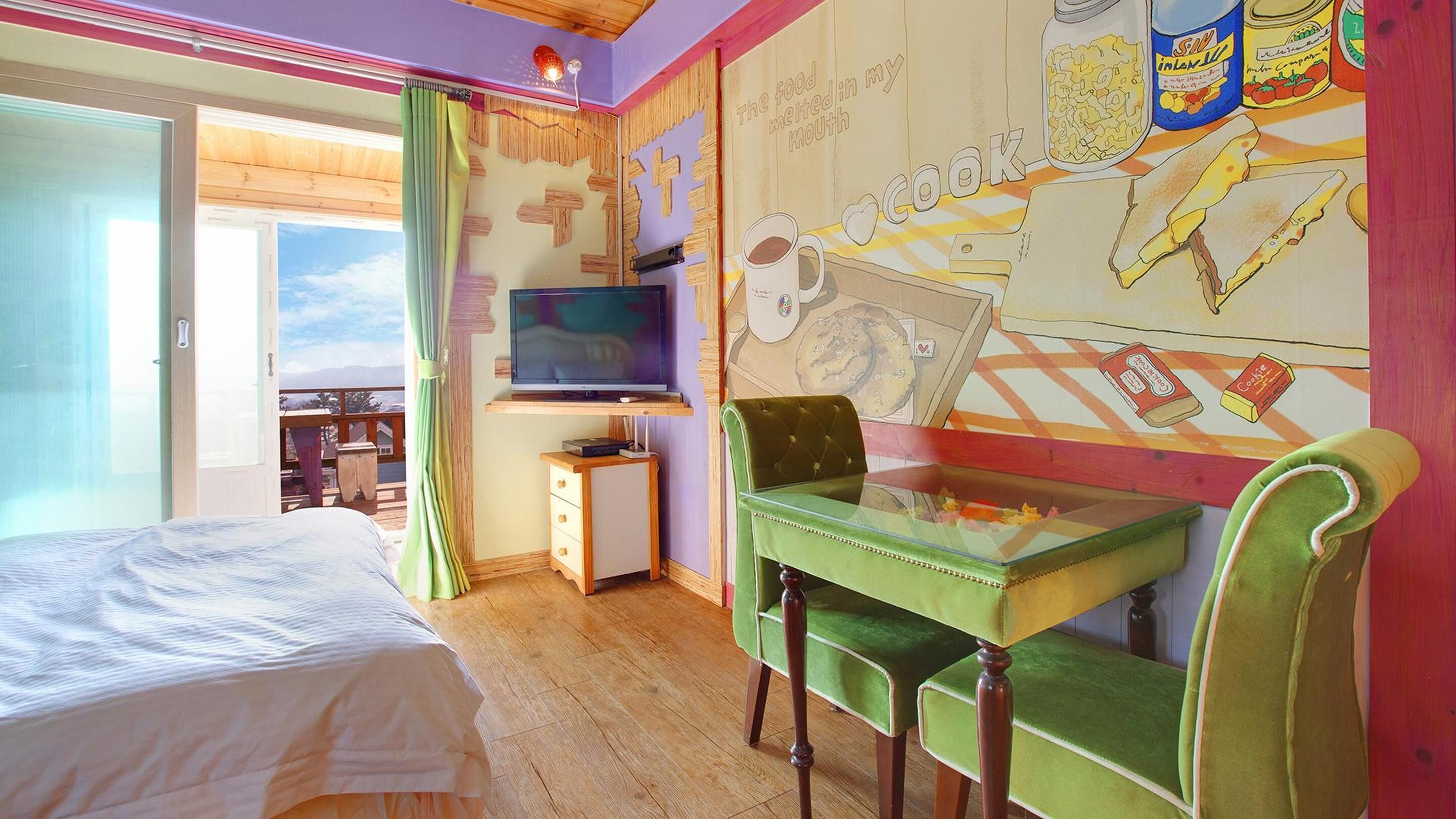 A bedroom with a bed, a TV, a desk with a chair, and a mural on the wall.