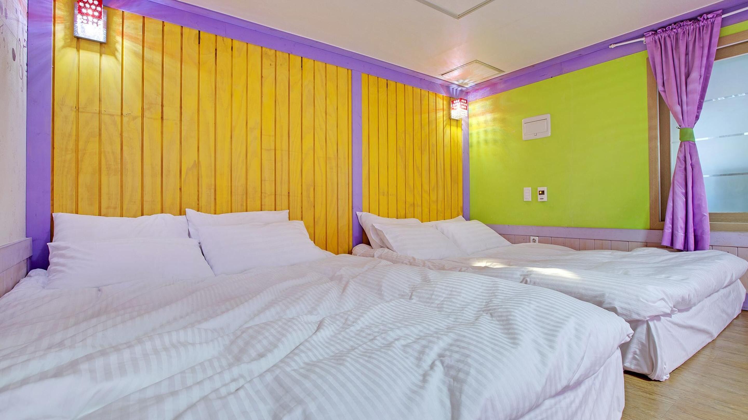 A hotel room with two beds, yellow and purple walls, and a green accent wall.