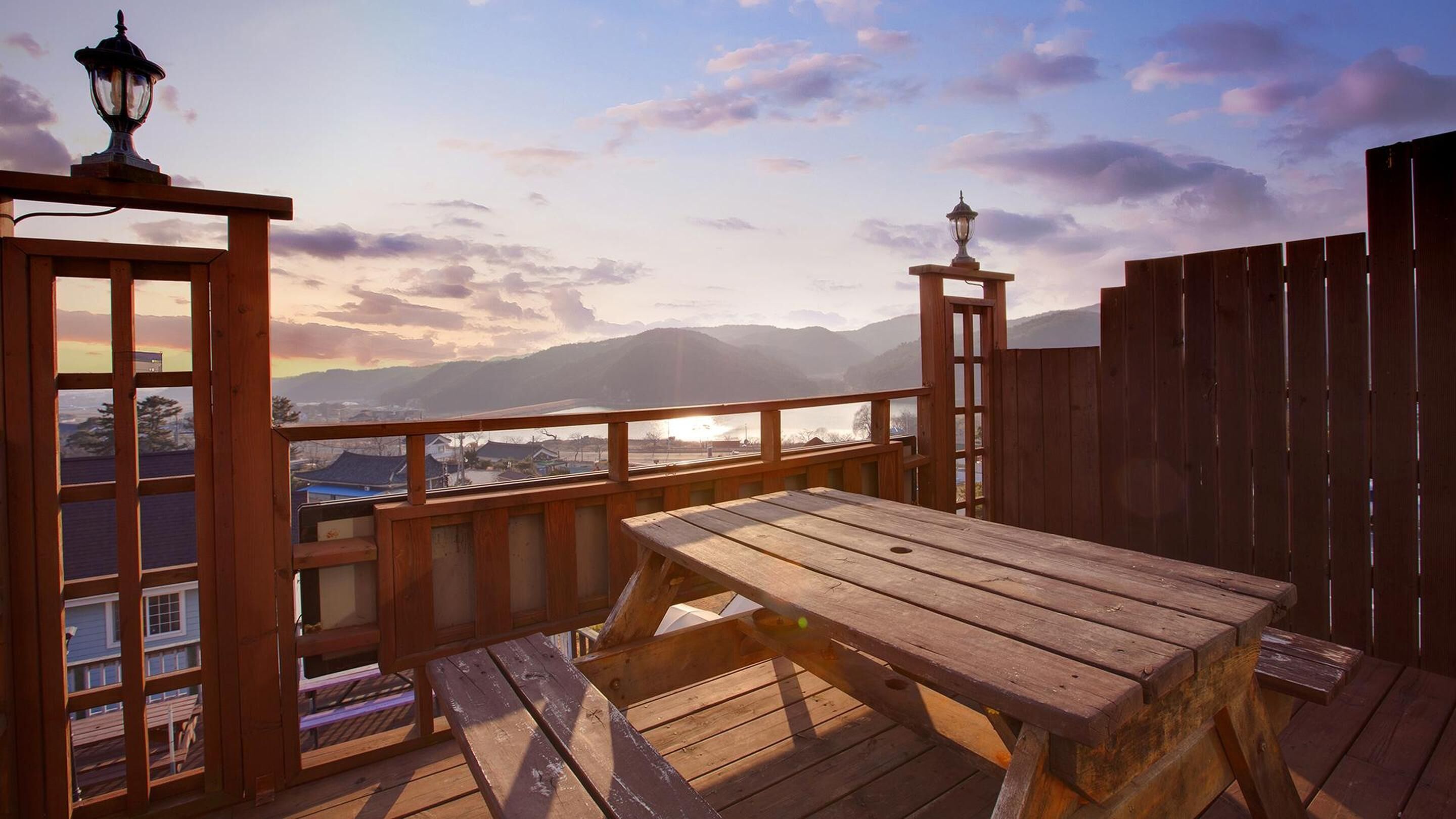 Una terraza de madera con una mesa y bancos, con vistas a un paisaje montañoso y un pueblo.
